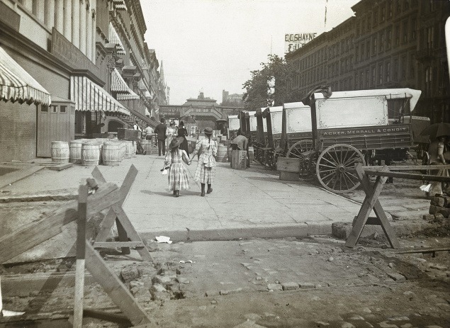 Okolo 1890: Dve dievčatá na prechádzke po 42. ulici. Po pravej strane stoja vozy dodávajúce víno do obchodov.