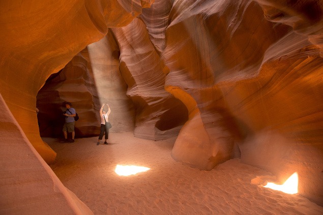Turisti fotografujú hru svetla prenikajúcu cez vápencové steny kaňonu Antelope v Arizone.
