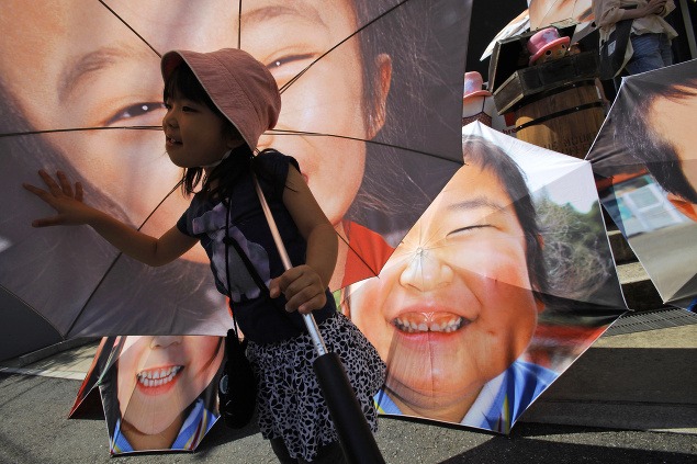 Dievča drží dáždnik s portrétom dieťaťa, ktoré prežilo minuloročné zemetrasenie a cunami v Japonsku.