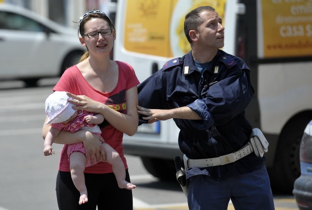 Taliansky policajt usmerňuje zdrvenú ženu s bábätkom v Mirandole.
