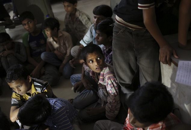 Malí indickí pracovníci sedia na podlahe mestského úradu po tom, čo ich zachránili pri razii v odevnej továrni.