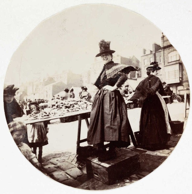 Žena pri stánku na trhovisku, okolo roku 1890.