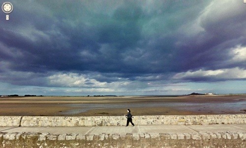 Žena kráčajúca po brehu mora. Búrka sa blíži.
