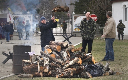 Ukrajinci si robia vatru zatiaľ čo ruský vojak stráži vchod do ukrajinskej vojenskej základne na Kryme