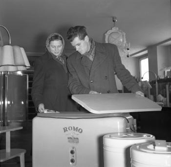 Manželia Šablicovci sa rozhodujú pre kúpu práčky značky ROMO v jednej z predajní počas predvianočného trhu v Bratislave. (1955)
