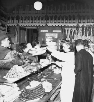 Zákazníci nakupujú v bratislavskej predajni Zdroj, ktorá ponúka bohatý výber rôznych druhov potravín a alkoholických nápojov počas vianočných trhov. (1950)