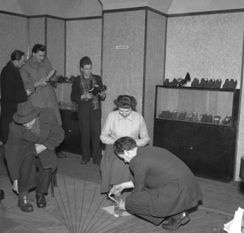 Zákazníci si skúšajú topánky, ktoré vyrobili Remeselné závody, kde šijú obuv na mieru. (1950) 