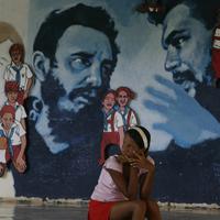 Mladé devča sedí pri múre s nástennou maľbou kubánskeho vodcu.