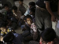 Malí indickí pracovníci sedia na podlahe mestského úradu po tom, čo ich zachránili pri razii v odevnej továrni.