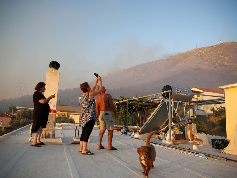 Miestni obyvatelia sledujú požiar zo strechy domu na aténskom predmestí Peania