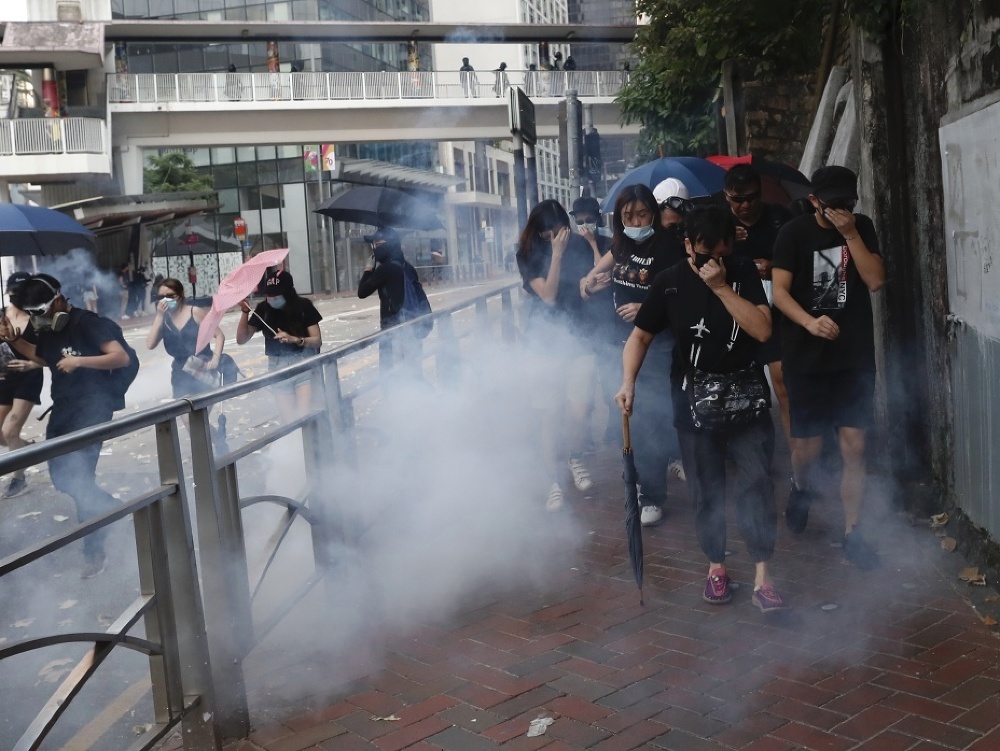 Ľudia si zakrývajú tvár pri zásahu polície slzotvorným plynom na demonštrantov počas protestu v Hongkongu