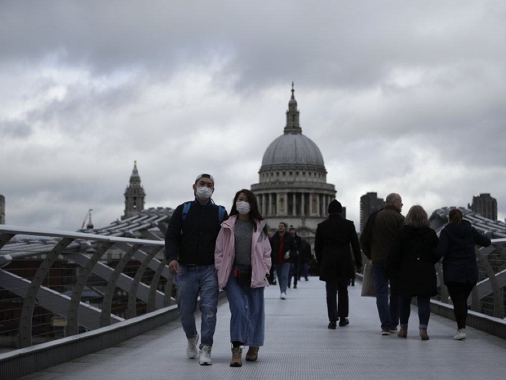 Ľudia s rúškami na tvárach kráčajú cez most pre peších London Millennium 10. marca 2020 v Londýne. 