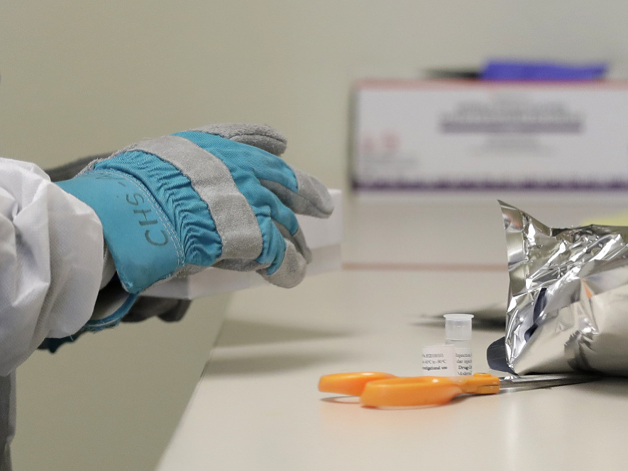 Lekár otvára v rukaviciach zmrazené balenie s vakcínou proti novému koronavírusu počas klinickej skúšky vakcíny