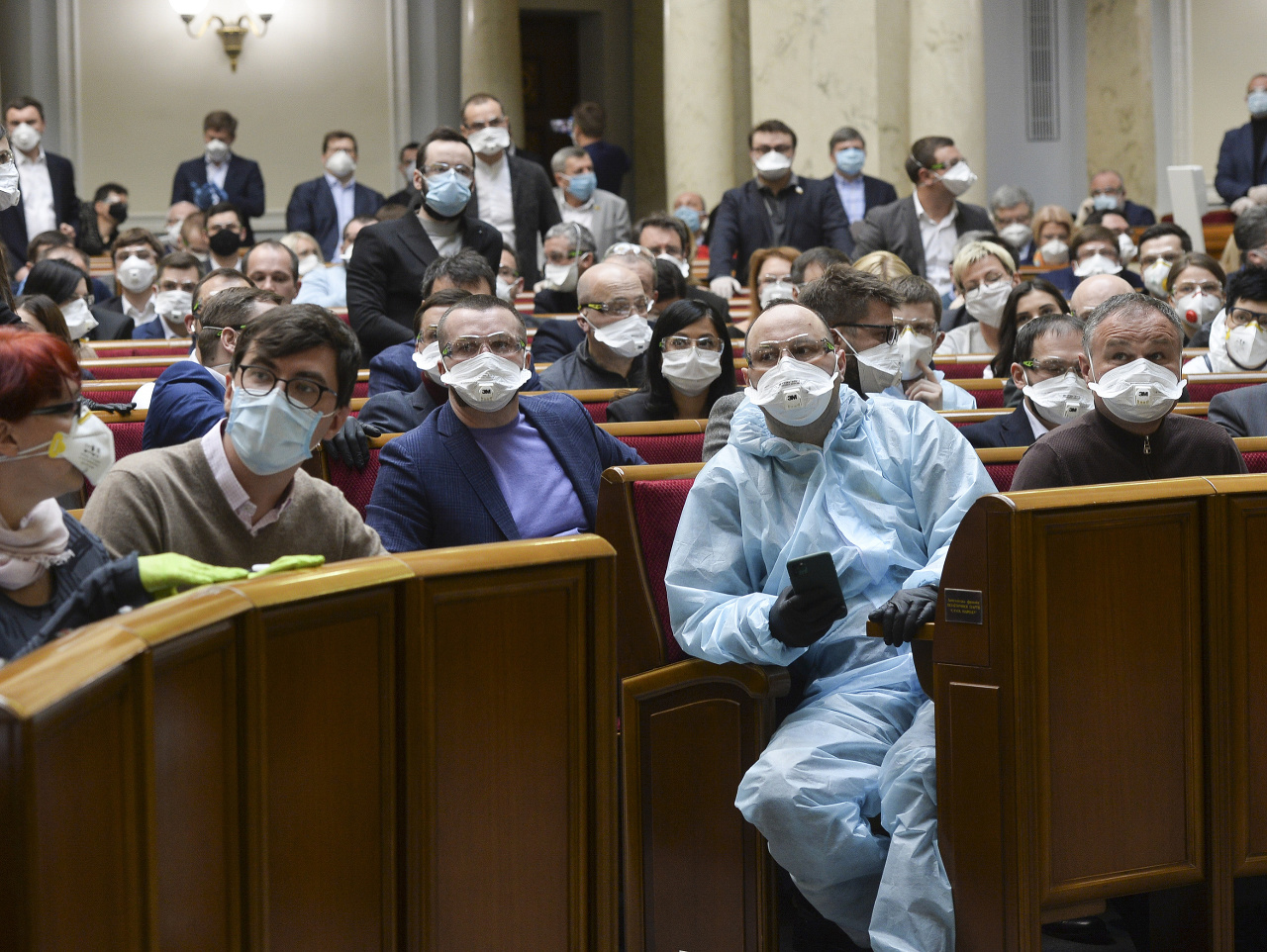Ukrajinskí poslanci s ochrannými rúškami a ochranným odevom sedia počas mimoriadneho zasadnutia parlamentu v Kyjeve
