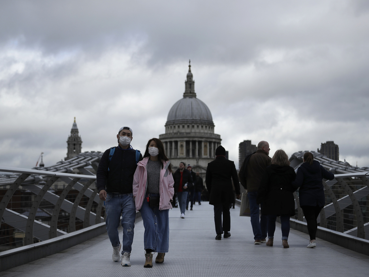 Ľudia s rúškami na tvárach kráčajú cez most pre peších London Millennium v Londýne. 