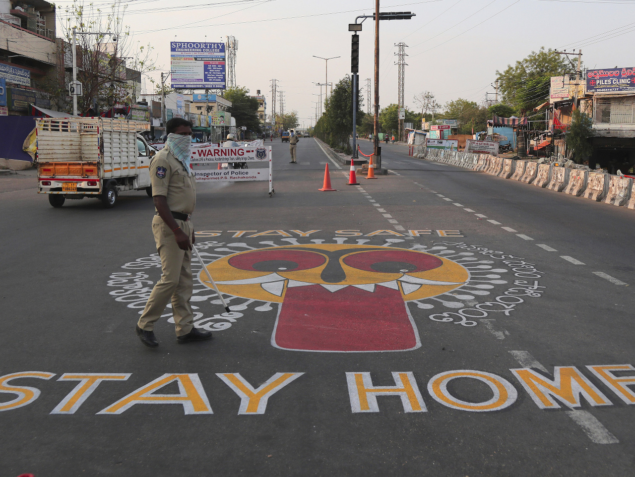 Policajt kráča okolo nápisu Zostaňte doma, ktorý sa nachádza na ceste v indickom meste Hajdarabád