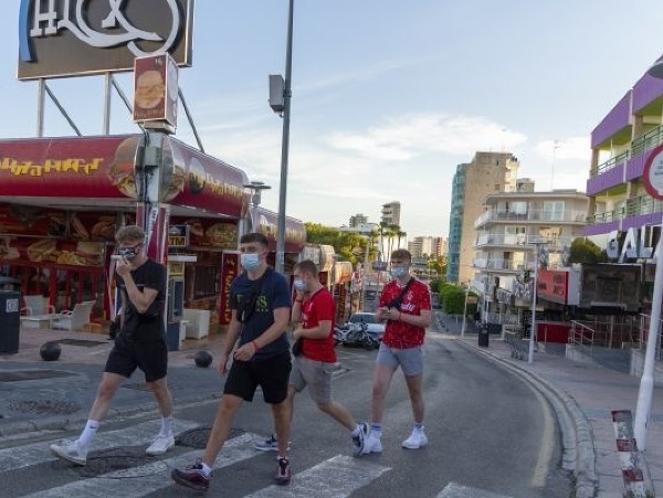Turisti s ochrannými rúškami kráčajú po ulici v letovisku Magaluf