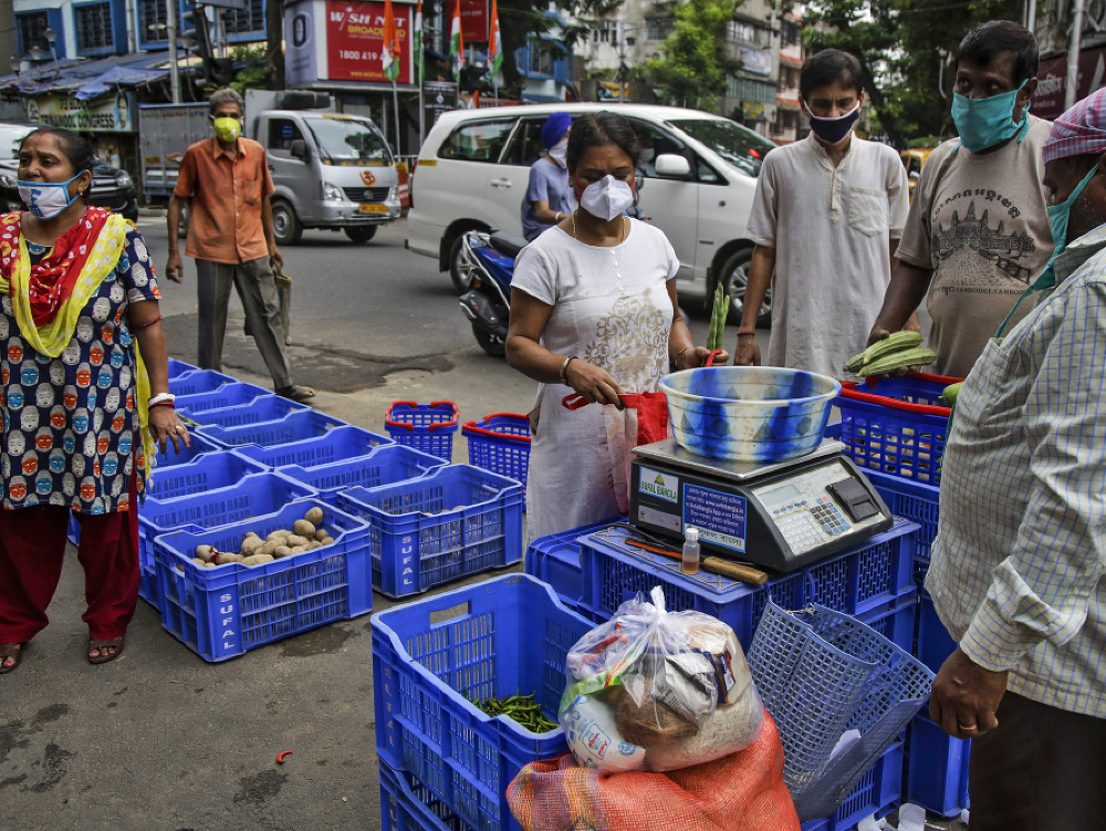 Ľudia s rúškami na tvárach nakupujú zeleninu na ulici v Kalkate v Indii