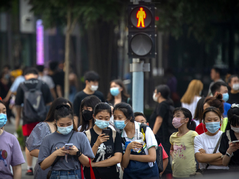 Ľudia s ochrannými rúškami čakajú na križovatke v čínskom Pekingu 