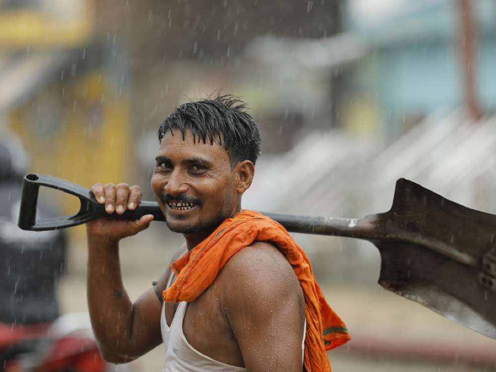 Indický robotník prechádza cez cestu počas monzúnového dažďa.
