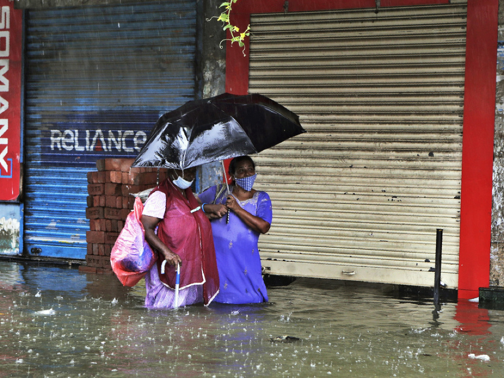Ľudia s ochrannými rúškami na zabránenie šíreniu nového koronavírusu sa pokúšajú prejsť cez zaplavenú ulicu počas silných dažďov v indickom Bombaji.