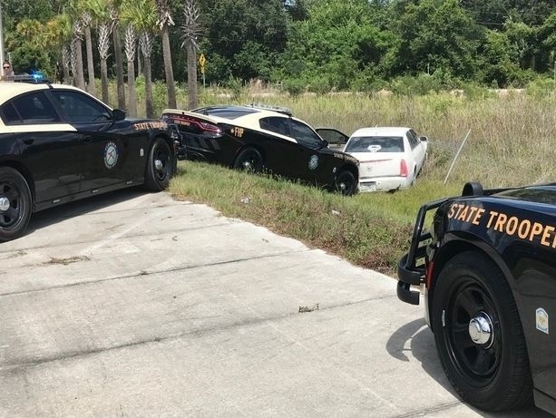 Cadillac skončil v drôtenom plote na trávnatom poraste obkľúčené policajnými autami.