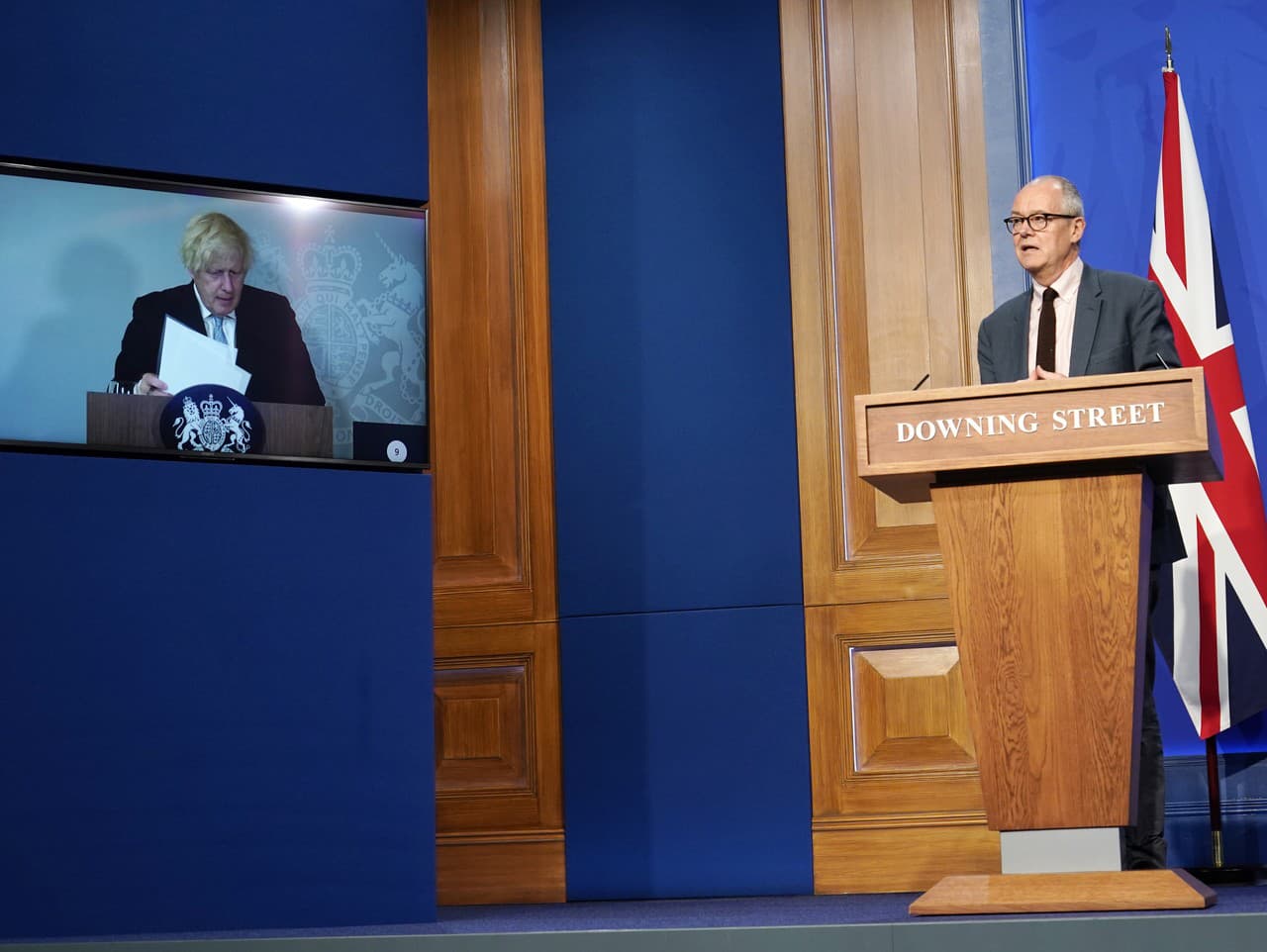 Hlavný vedecký poradca britskej vlády Patrick Vallance (vpravo) a britský premiér Boris Johnson, ktorý je na televíznej obrazovke z dôvodu domácej izolácie.