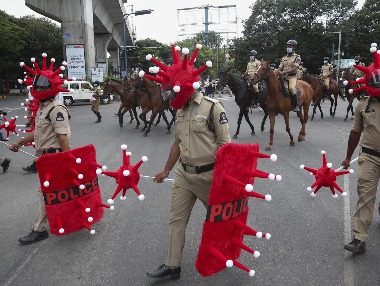 Indickí policajti kráčajú v prilbách v tvare nového typu koronavírusu počas akcie zameranej na prevenciu jeho šírenia.