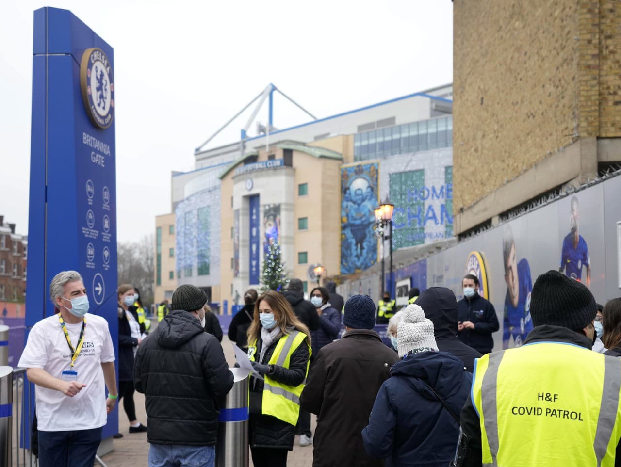 Ľudia čakajú na očkovanie na štadióne Stamford Bridge, ktorý je domovským stánkom futbalového klubu Chelsea Londýn
