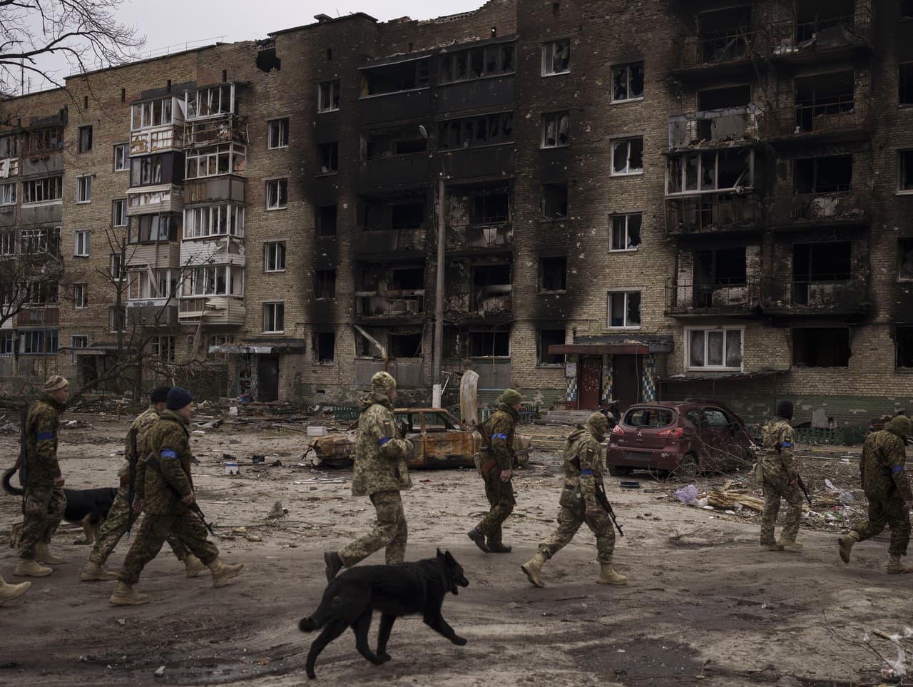 Ukrajinskí vojaci kráčajú popri ťažko poškodených obytných budovách v Irpine.