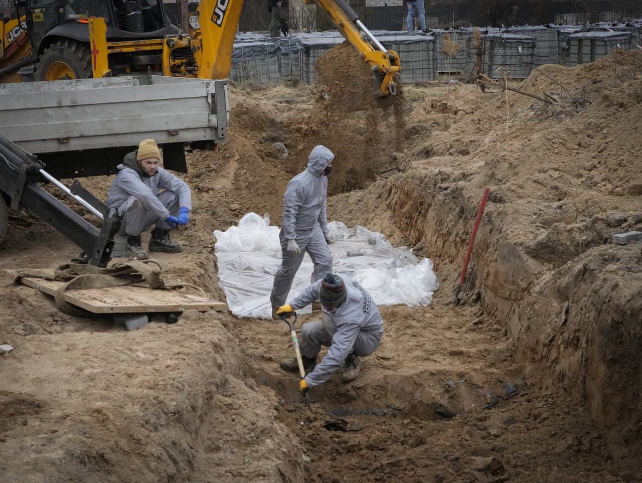 Muži v ochranných výstrojoch exhumujú telá civilistov.
