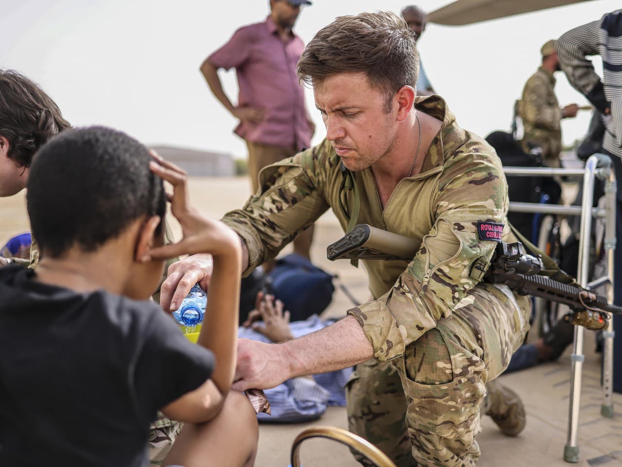 Evakuácia obyvateľov Sudánu. Príslušník štátnej armády ponúka vodu malým deťom na vojenskom letisku. 