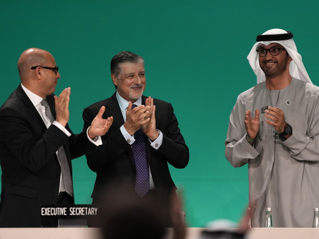 Prezident COP28 Sultán Ahmad al-Džábir (vpravo) tlieska s výkonným riaditeľom COP28 Adnanom Aminom (uprostred) a klimatickým šéfom OSN Simonom Stiellom (vľavo) po dohode na odklone od fosílnych palív