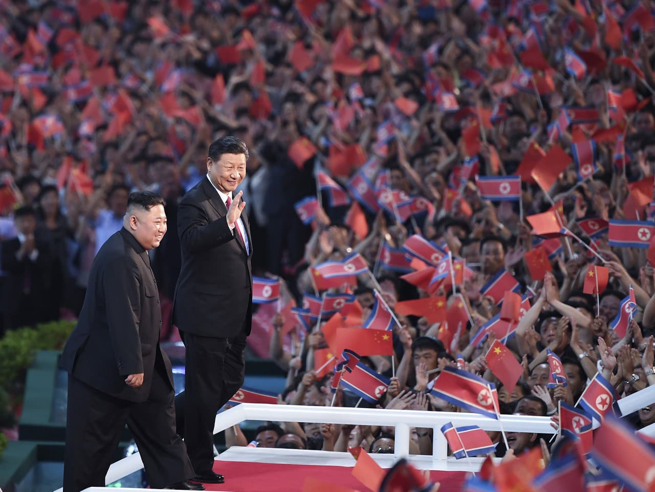 Na snímke severokórejský vodca Kim Čong-un (vľavo) a čínsky prezident Si Ťin-pching mávajú divákom počas hromadného gymnastického vystúpenia v Pchjongjangu