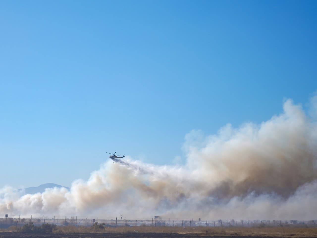 Vrtuľník zhadzuje vodu pri hasení požiaru Max Fire, nedeľa 16. júna 2024, Lancaster, Kalifornia