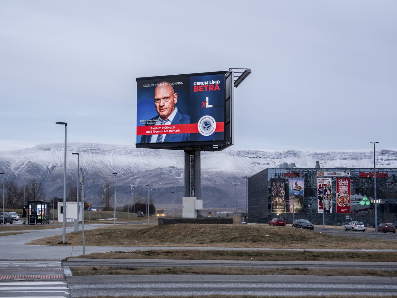 Billboard Demokratickej strany (Lýðræðisflokkurinn) s nápisom „Obmedzme úrokovú sadzbu zákonom na maximálne 4 %“. V pozadí je hora Esja pokrytá čerstvým snehom v Reykjavíku na Islande.