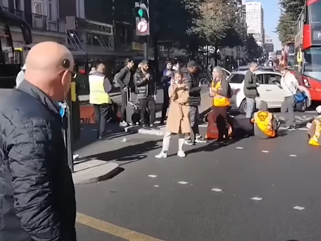 Vodič vystupuje z auta a bezmocne kričí po protestujúcich, ktorí zablokovali cestu. 