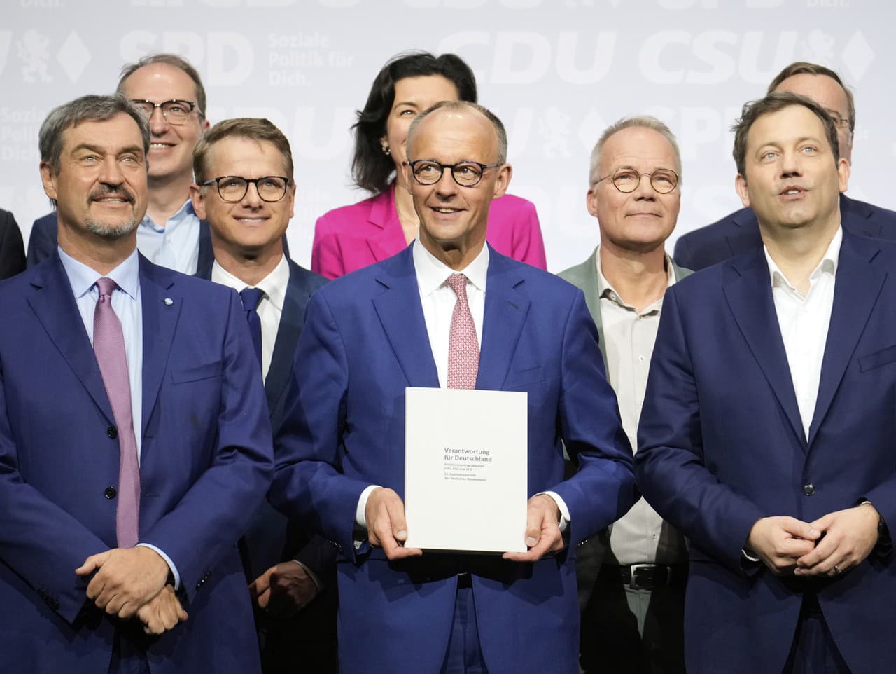 Líder CSU Markus Soeder, líder CDU Friedrich Merz a líder SPD Lars Klingbeil (v prvom rade zľava) stoja spolu s novými ministrami po podpise koaličnej zmluvy.