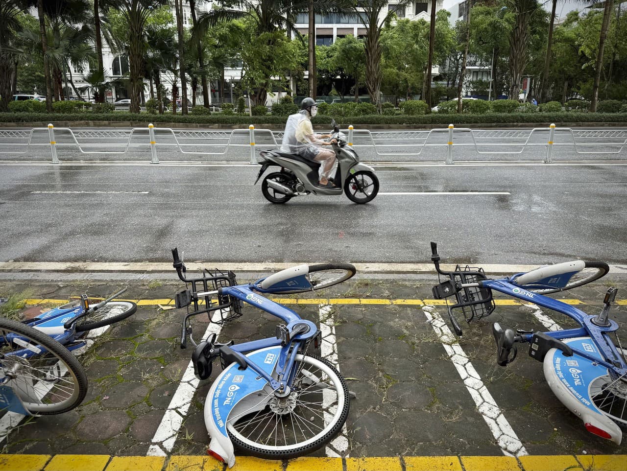 Motocyklista jazdí v daždi okolo spadnutých bicyklov po búrke Wipha v Hanoj
