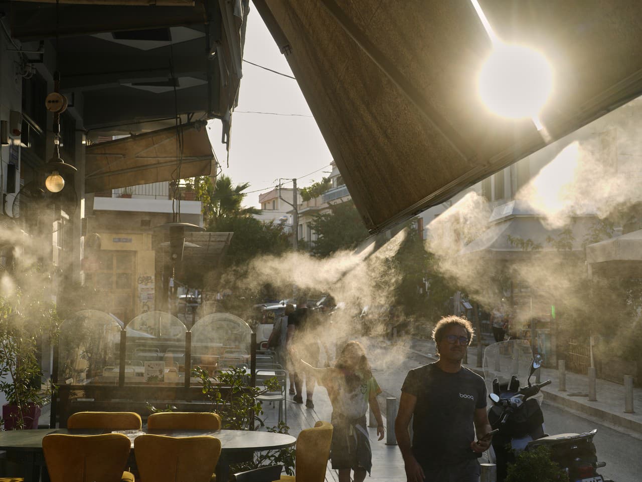 Ľudia kráčajú vedľa vodnej hmly v aténskej štvrti Thisio počas horúčav