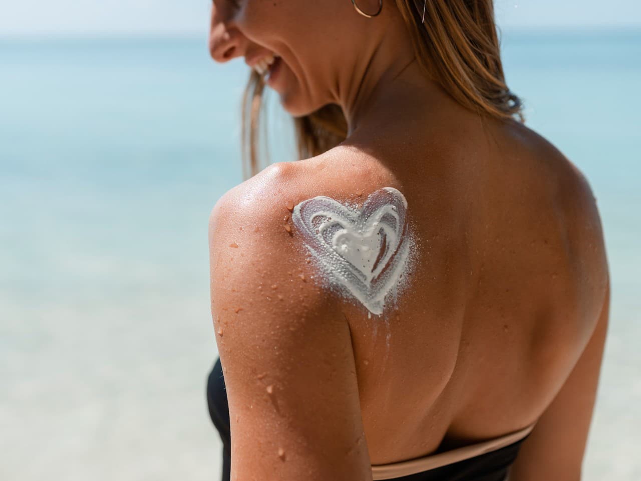 Žena srdcom z opaľovacieho krému na ramene pri mori