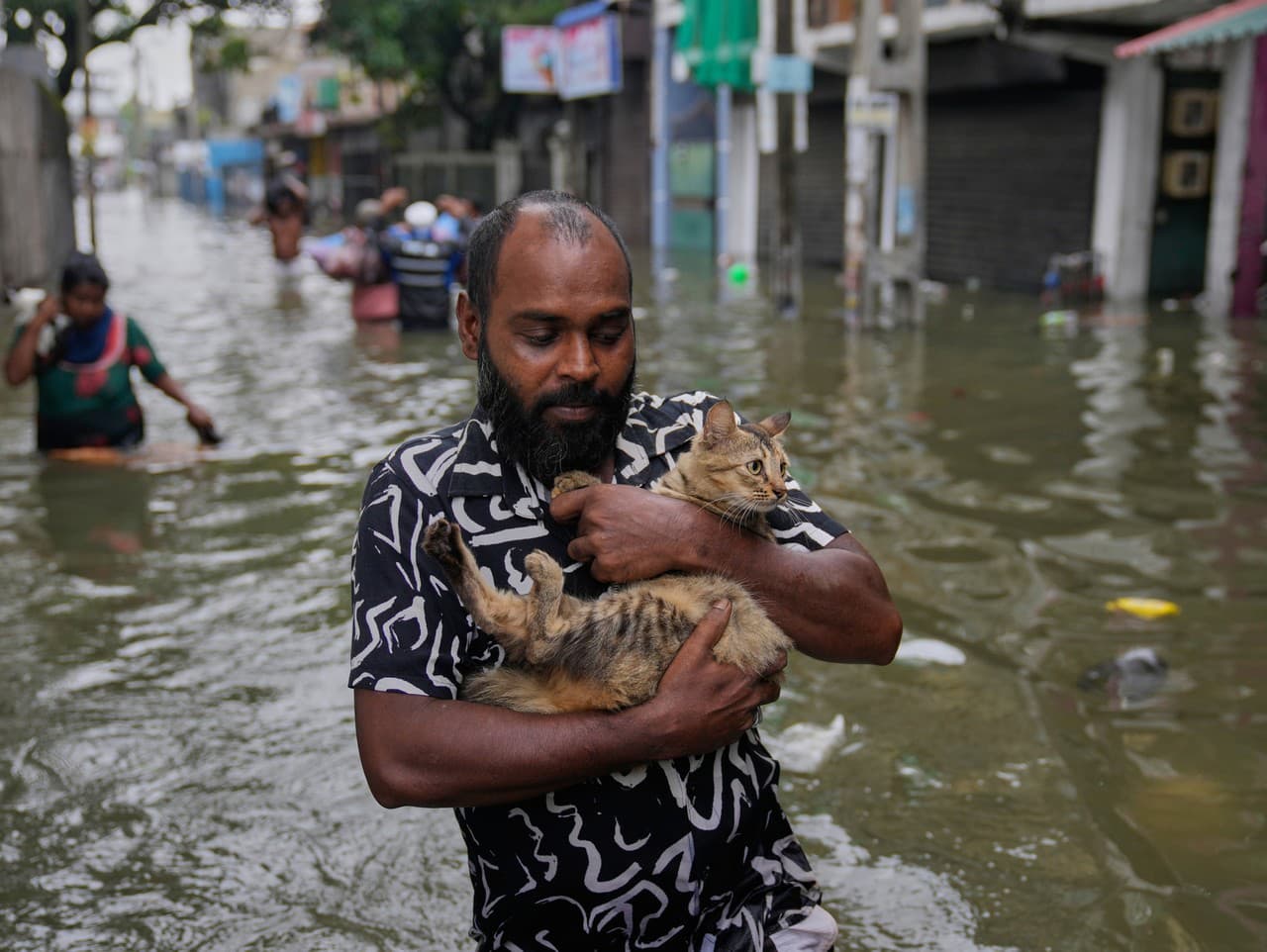 Muž sa brodí po zaplavenej ulici s mačkou v náručí v Kolombe.