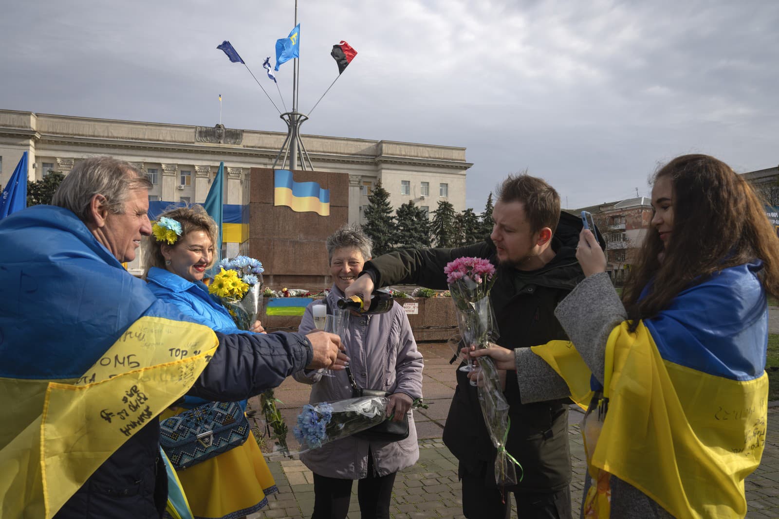 Obyvatelia mesta zahalení v štátnych vlajkách pijú šampanské a držia kvety pri príležitosti jedného roka od znovudobytia mesta Cherson ukrajinskými okupačnými silami na centrálnom námestí v ukrajinskom Chersone