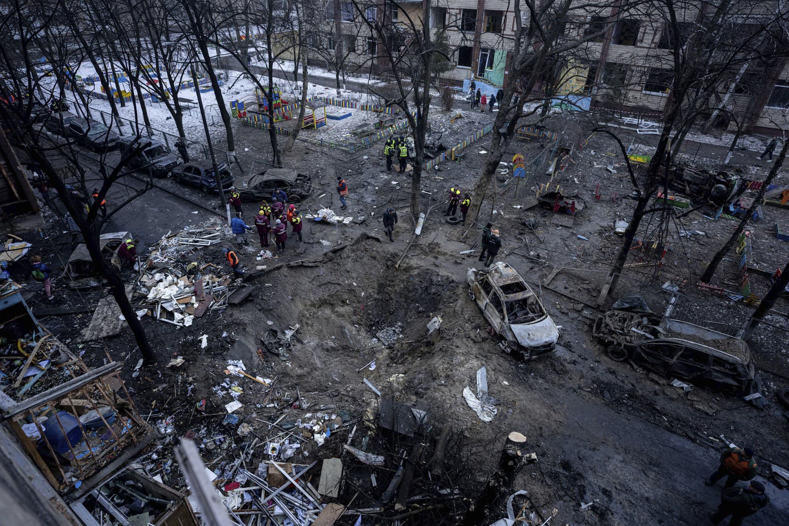 Ľudia stoja pri kráteri na dvore poškodenej viacpodlažnej budovy po ruskom útoku na obytnú štvrť v Kyjeve na Ukrajine v stredu 13. decembra 2023.