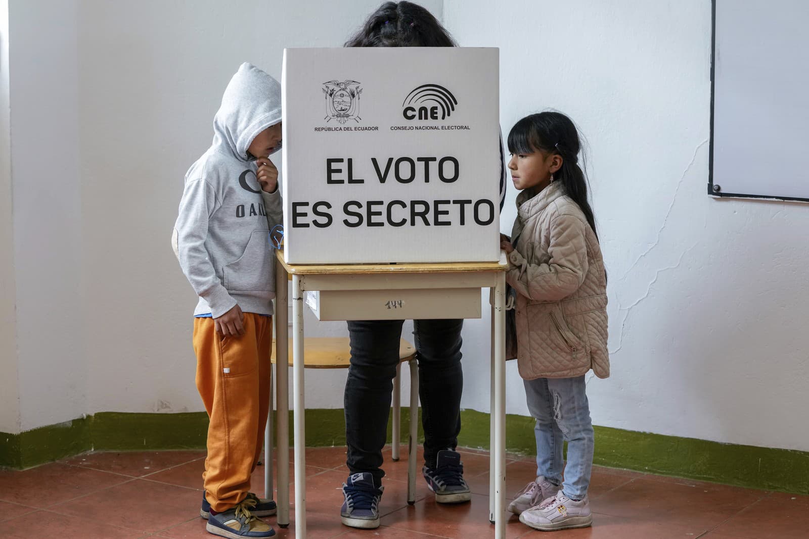 Deti stoja pri voličke, ktorá označuje otázky na hlasovacom lístku referenda navrhnutého prezidentom Danielom Noboaom na schválenie nových bezpečnostných opatrení zameraných na potlačenie zločineckých gangov, ktoré podnecujú eskaláciu násilia v ekvádorskom Quite