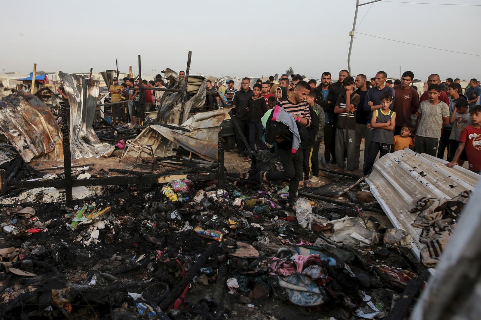 Palestínčania sa pozerajú na zničené miesto po izraelskom útoku, kde sa zdržiavali vysídlení ľudia v Rafahu v pásme Gazy v pondelok 27. mája 2024.