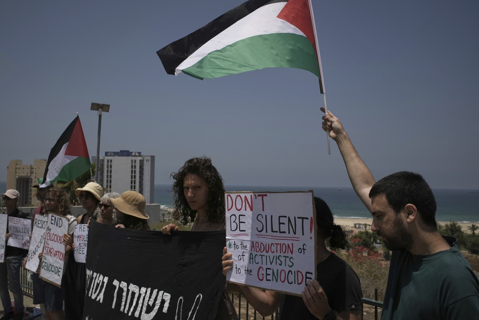 Ľudia mávajú palestínskou vlajkou a držia transparenty na podporu Grety Thunbergovej a ďalších aktivistov, ktorí sa pokúšali doručiť pomoc do Gazy predtým, ako ich loď zadržali izraelské sily, neďaleko prístavu Ašdod v Izraeli v pondelok 9. júna 2025.