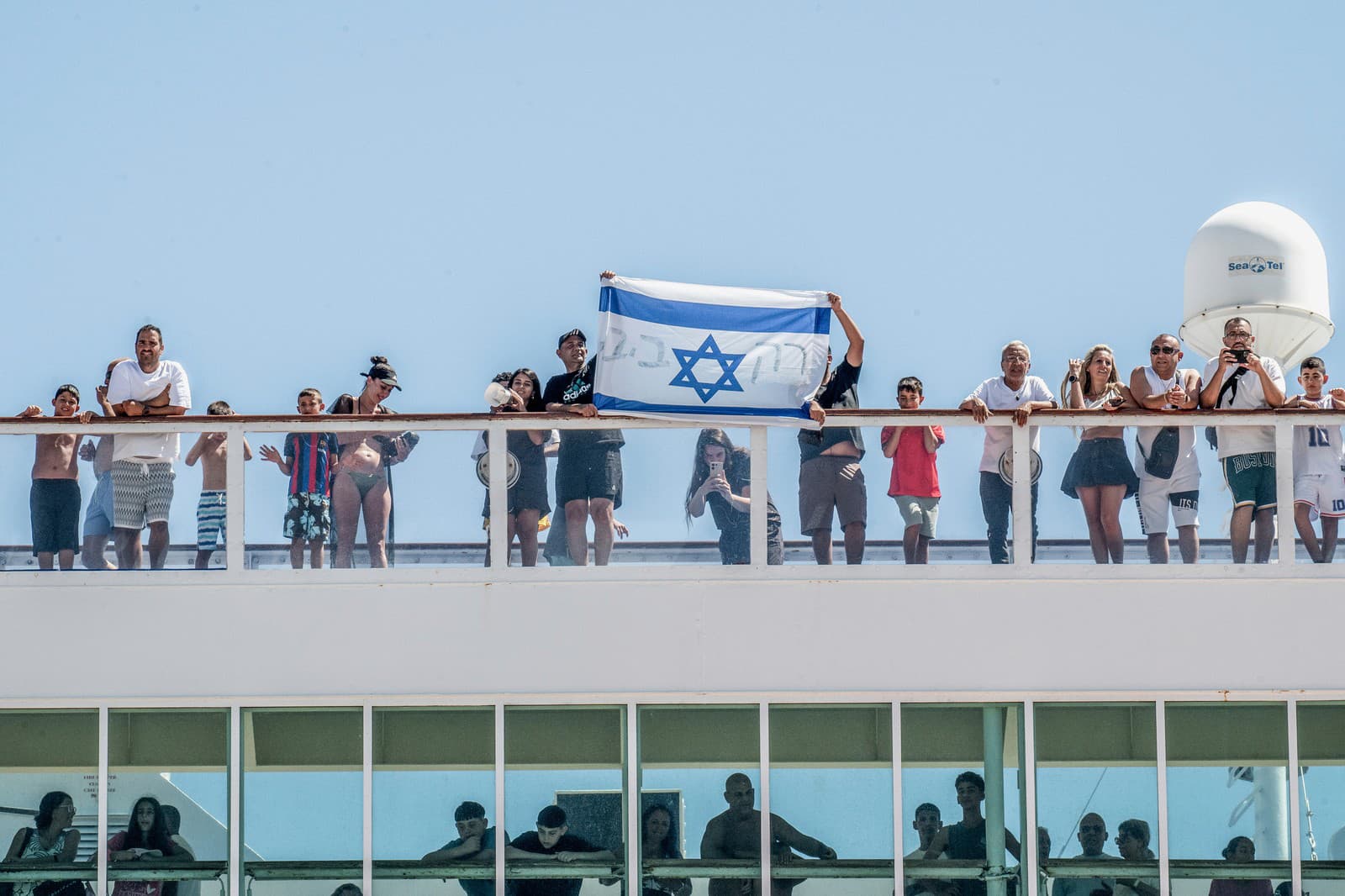 Izraelskí turisti držia vlajku svojej krajiny počas príchodu lode do prístavu Agios Nikolaos na ostrove Kréta