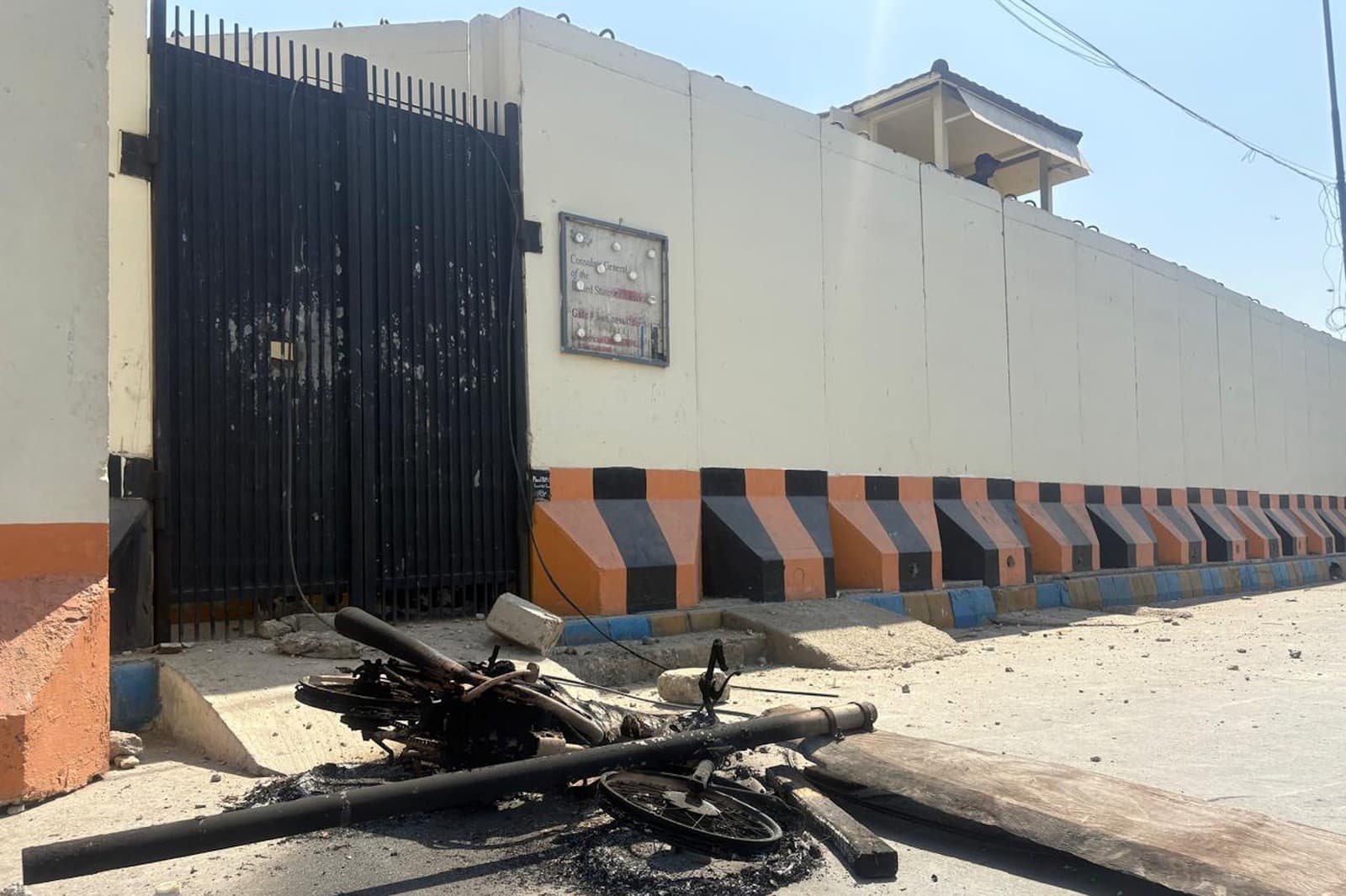 Bezpečnostný pracovník zaujal pozíciu, keď pred americkým konzulátom v pakistanskom Karáčí, ktorý protestujúci napadli, stojí motocykel zapálený rozzúrenými demonštrantmi.