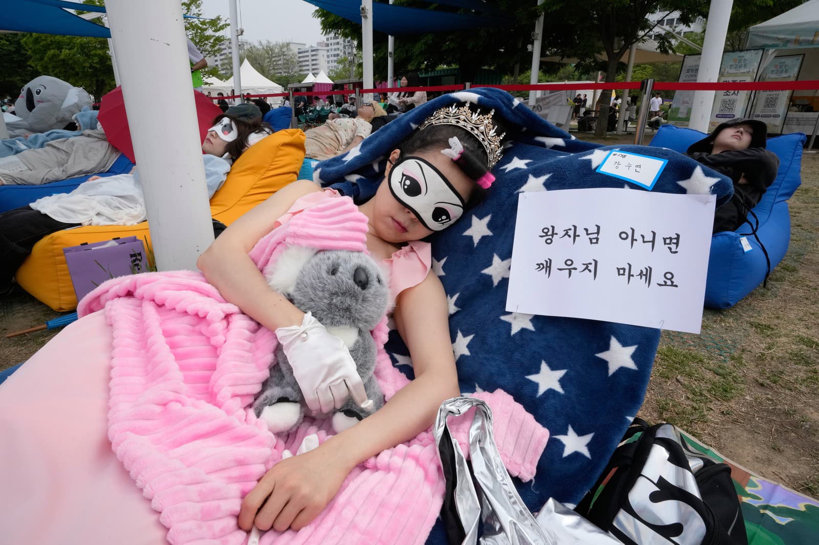 Účastník si zdriemne počas súťaže v zdriemnutí „Hangang Nap Competition 2026“ v parku Yeouido Hangang v Soule v Južnej Kórei v sobotu 2. mája 2026. Na nápise je napísané: „Nezobúdzaj ma, pokiaľ to nie je princ.“
